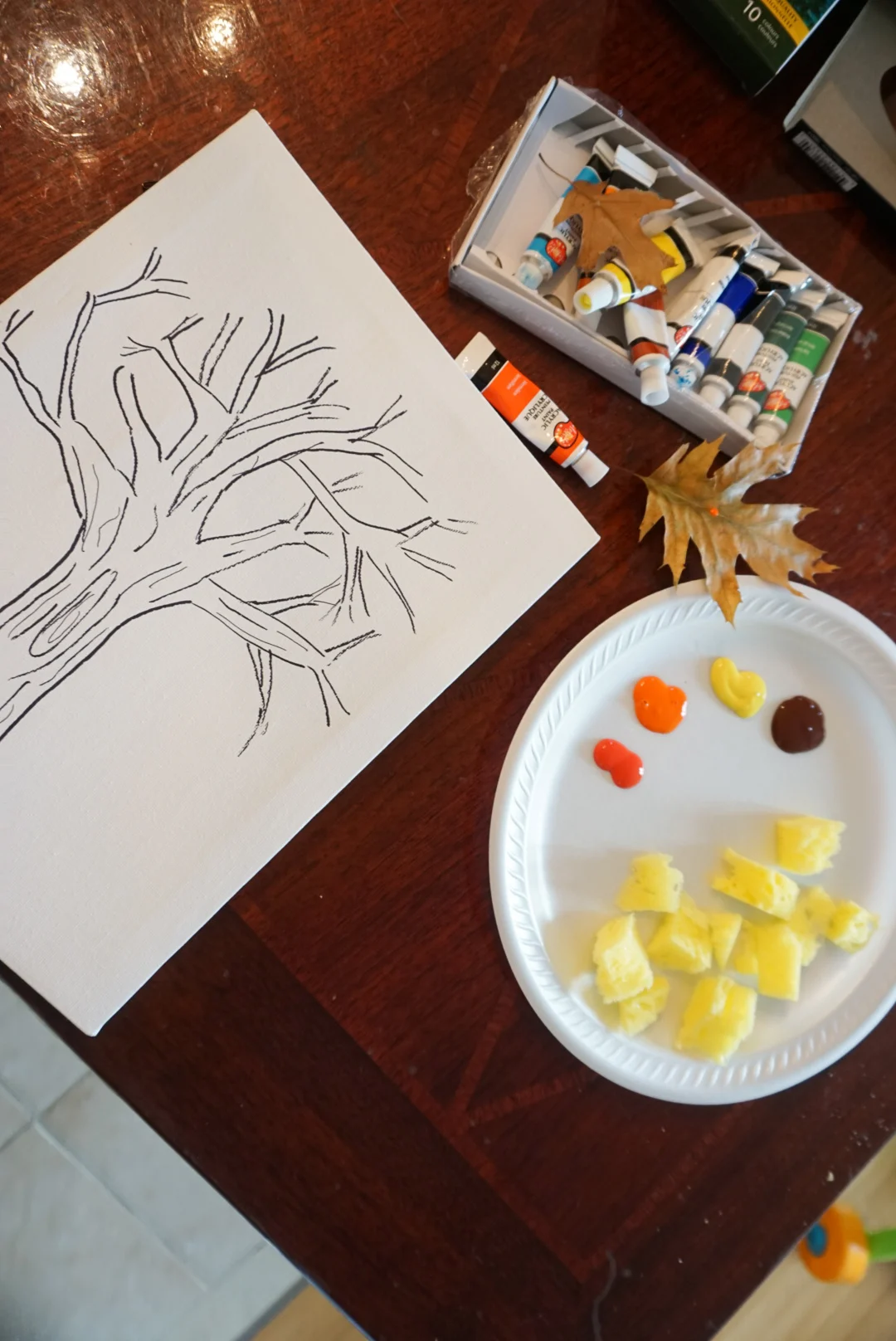 Painting supplies like paint, paint brush, paint sponges, canvas with a  tree drawing.