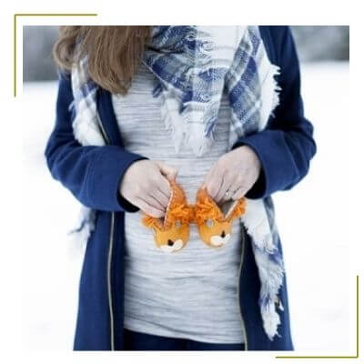 winter pregnancy announcement idea woman holds baby winter shoes in snow