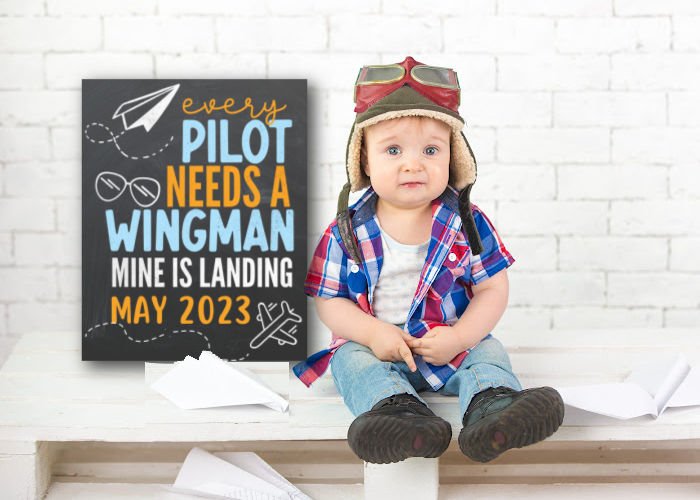 baby boy in pilot hat and goggles sitting next to pilot themed baby announcement sign 