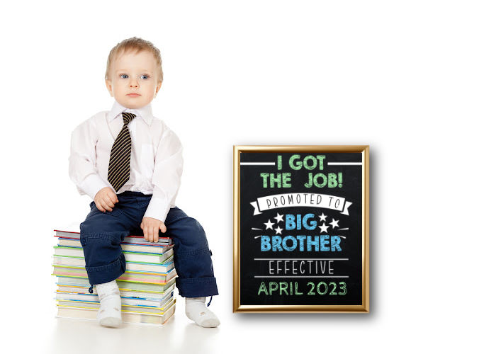 toddler boy dressed like adult in tie an dress shirt sitting next to 'promoted to big brother' announcement sign