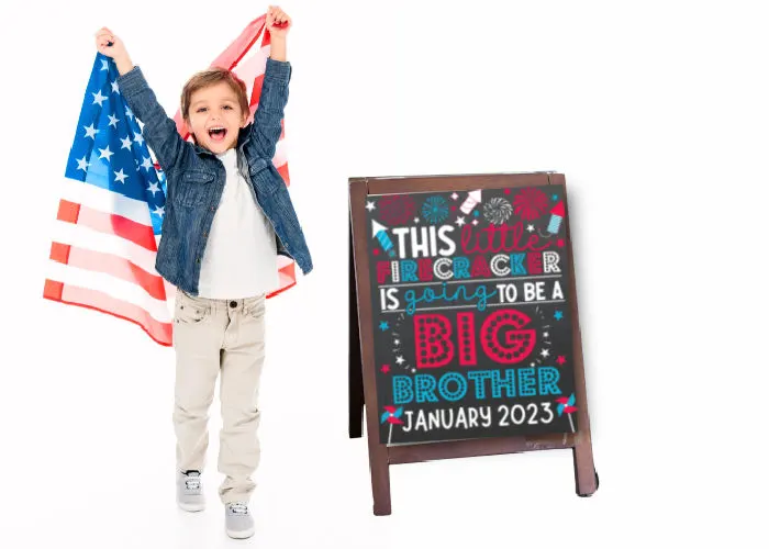 little boy holding American flag next to 4th of July big brother announcement sign