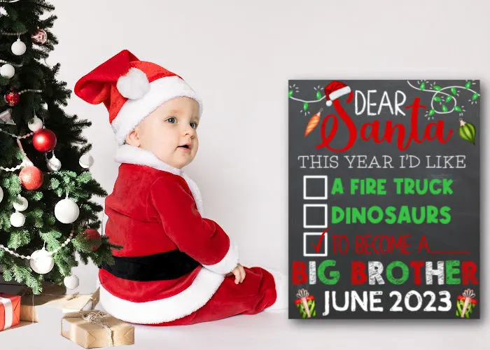 baby dressed like santa sitting next to Christmas tree and Christmas pregnancy announcement sign