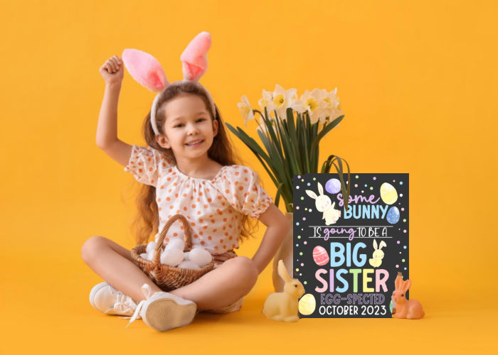 little girl wearing rabbit ears sitting next to Easter sibling pregnancy announcement that says she will be a big sister
