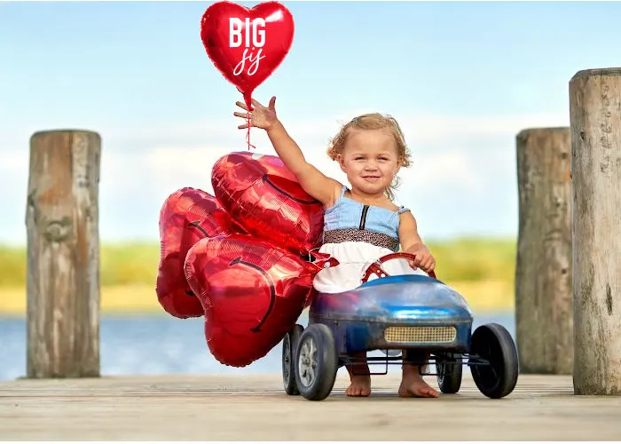 toddler girl in toy car holding 'big sis' balloon for pregnancy reveal 