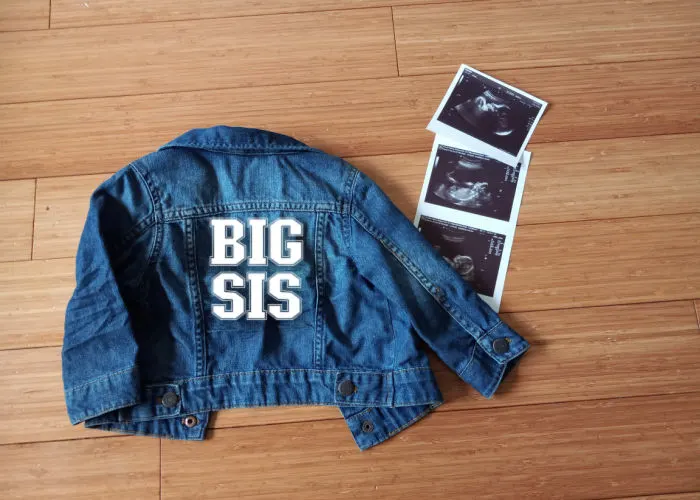 flat lay of big sis jean jacket and baby sonogram photos