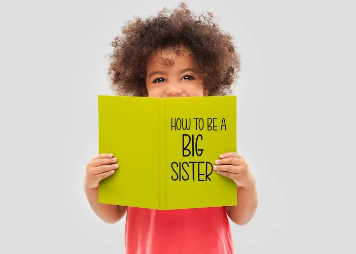 little girl holding 'how to be a big sister' book