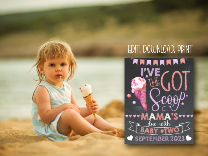 toddler girl at the beach eating ice cream, sitting in sand next to ice cream big sister announcement sign