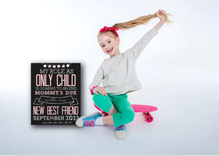 little girl sitting on a skateboard next to new best friend sibling announcement sign