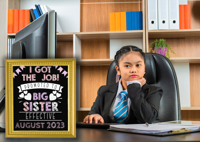 little girl dressed like boss sitting at table with computer next to promoted to big sister pregnancy announcement sign