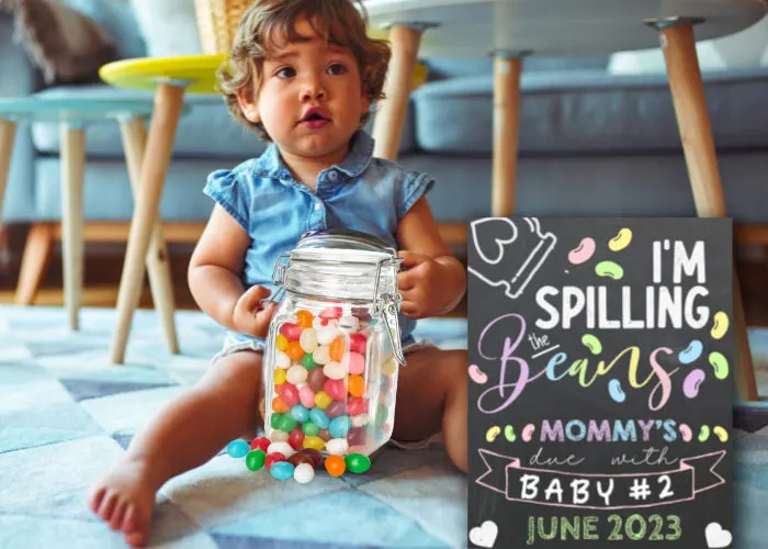 little girl holding jar of beans sitting next to jellybean themed pregnancy announcement sign