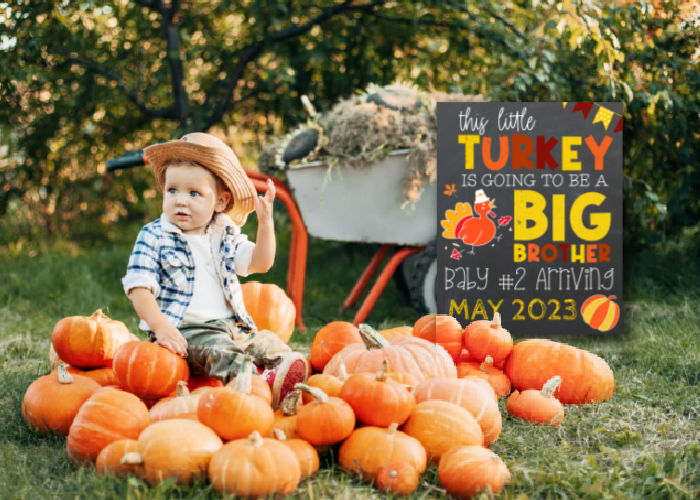 baby boy sitting in pumpkin patch next to Thanksgiving big brother announcement board