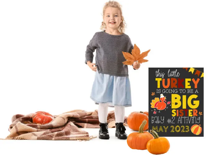 cute little girl holding leaf and surrounded by pumpkins standing next to thanksgiving big sister announcement board