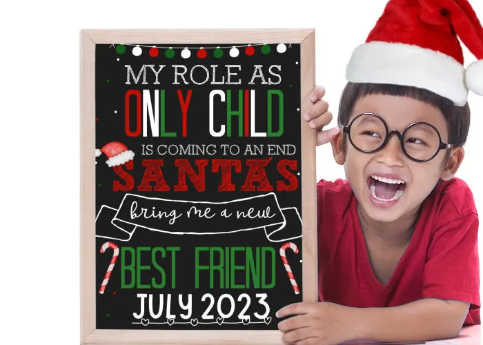 little boy in Santa hat holding a Christmas pregnancy announcement that reads my role as only child is coming to an end. Santa's bring me a new best friend.