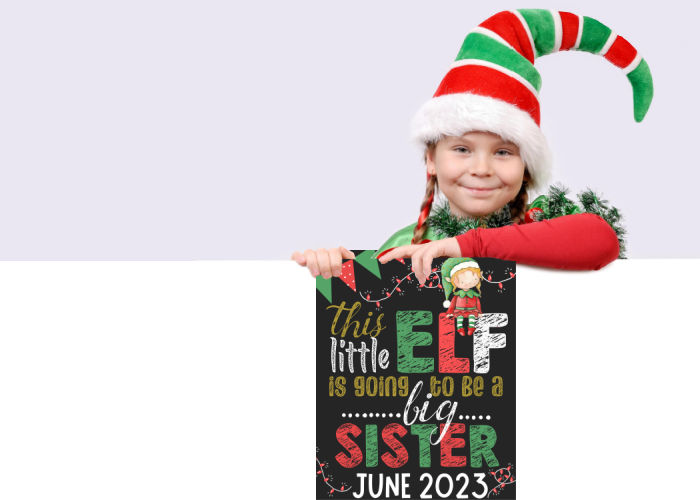 little girl dressed like elf holding elf Christmas pregnancy announcement chalkboard big sister sign