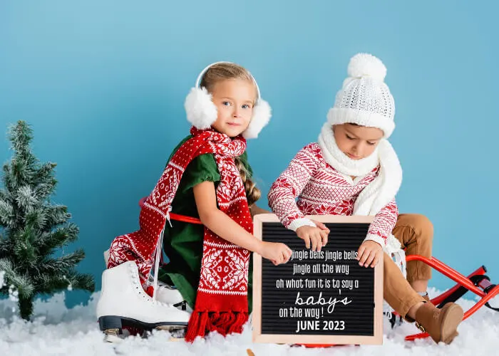 siblings sitting in sleigh with jingle bells baby announcement sign