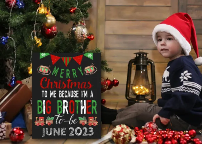 little boy wearing Santa hat sitting next to Christmas tree and big brother Christmas announcement 'merry Christmas to me because I'm a big brother to be'