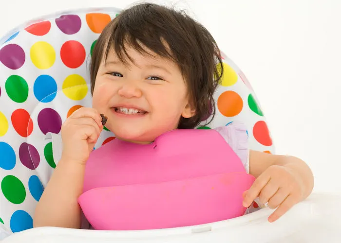baby in highchair with silicone bib eating.