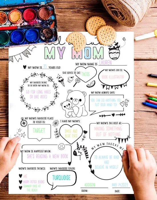 flat lay of all about mom printable worksheet with childs hands holding paper and table littered with pencil crayons, paint and crackers.