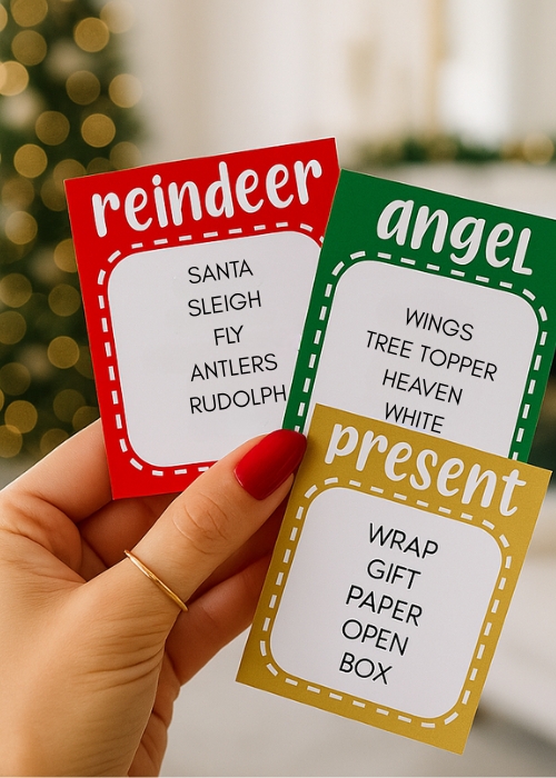 a manicured hand with red nails is holding up Chrismas taboo cards in front of  a christmas living room