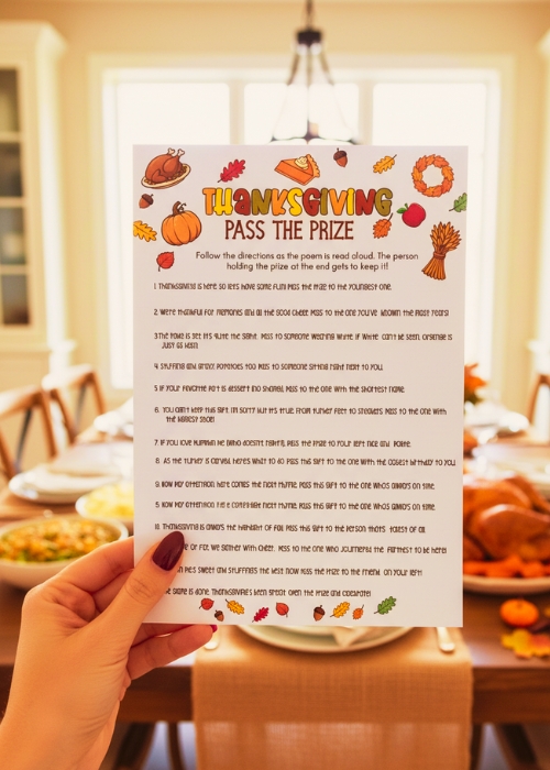 awoman's hand is holding up the Thanksgiving Pass The Prize game printable. She is at the Thanksgiving dinner table with a feast in the background. 