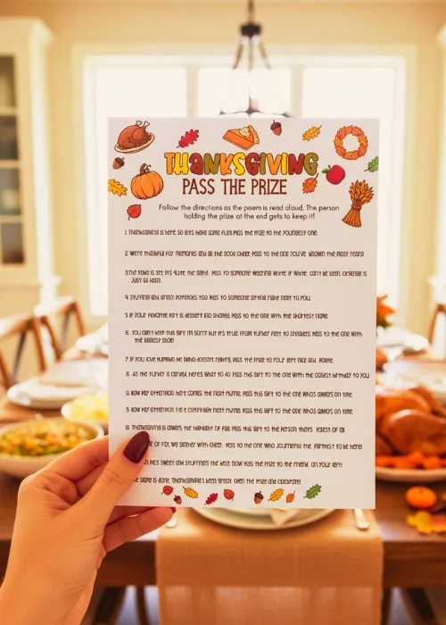 awoman's hand is holding up the Thanksgiving Pass The Prize game printable. She is at the Thanksgiving dinner table with a feast in the background.