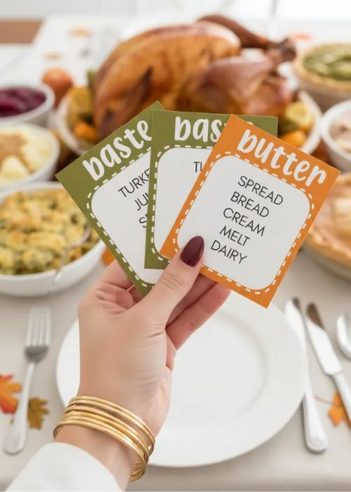 a woman's hand is holding up Thanksgiving Taboo game cards at the dinner table