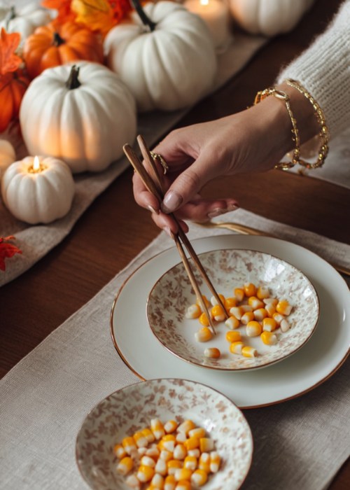 close up of a hand using chop sticks to move kernal corns for a thanksgiving party game
