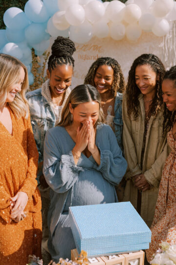a mom is surprised as she opens gifts at her shower surronded by friends